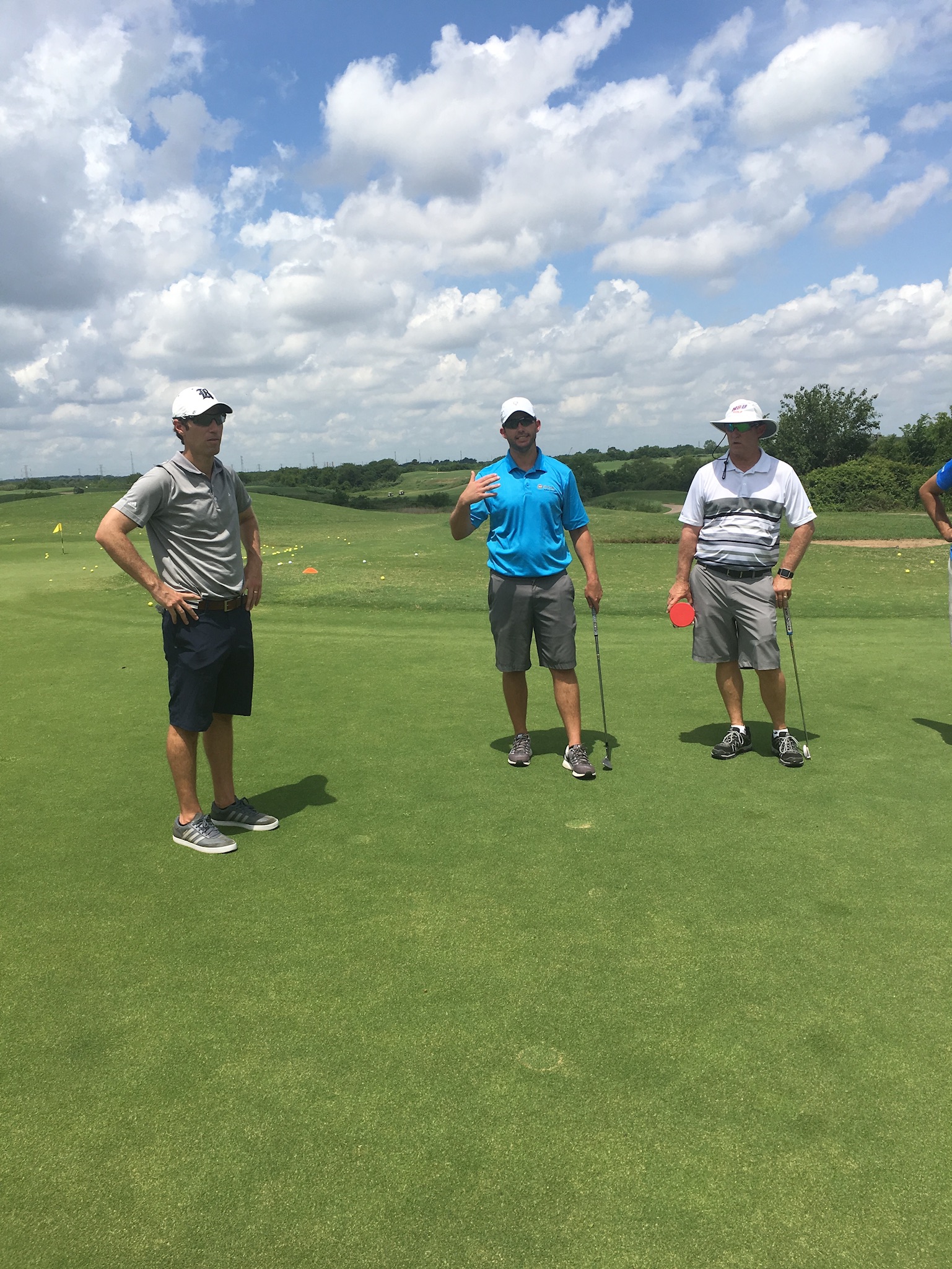 Three golf coaches in discussion on a practice range