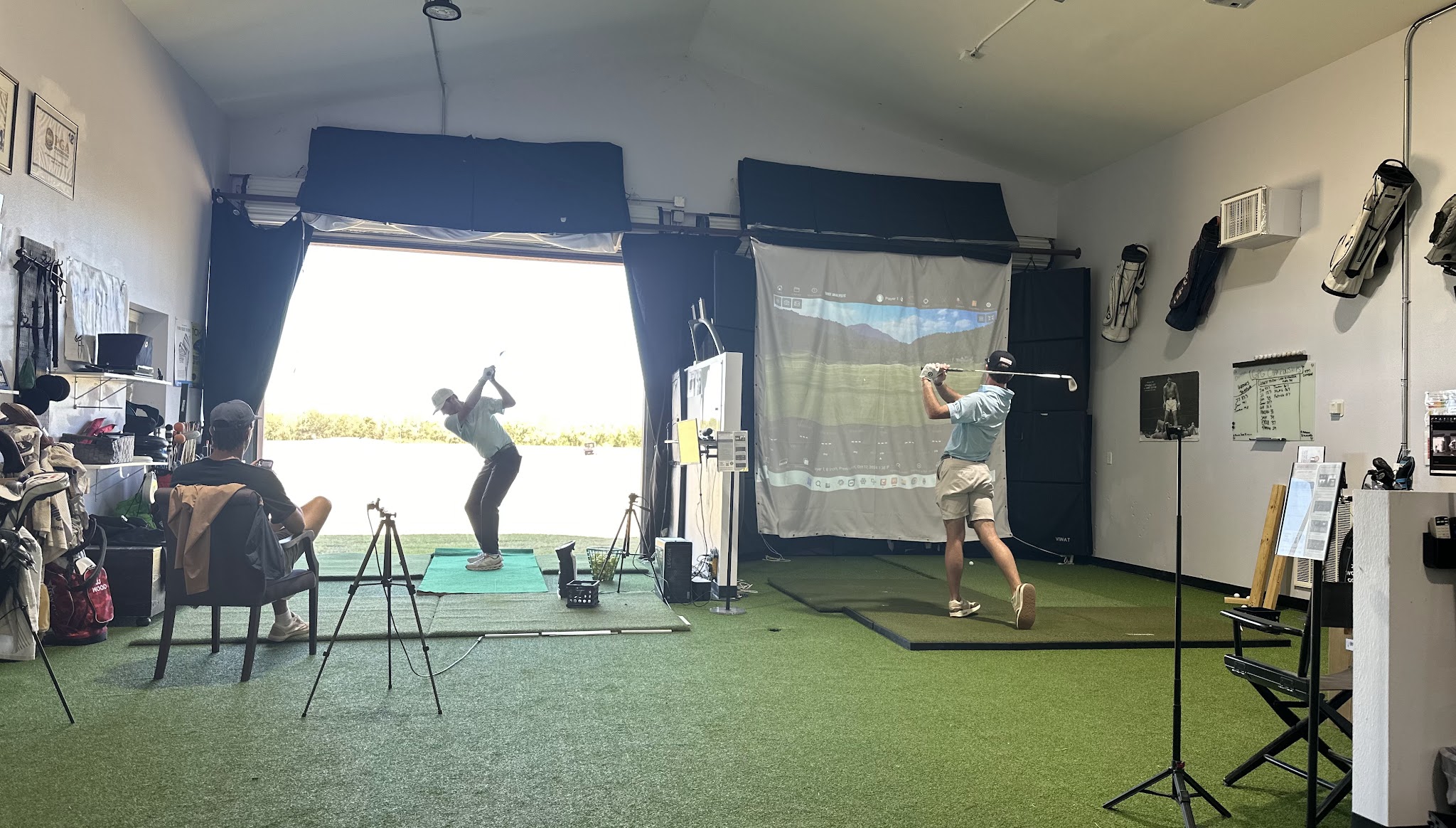 Two golfers practicing in adjacent indoor bays at Golf Performance Group